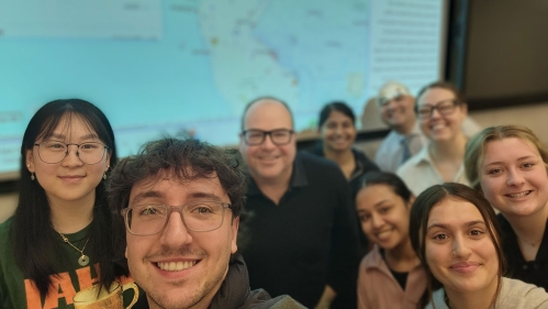 A professor and a group of students standing in front of a map.