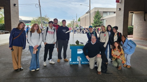 A group of students and a faculty member posing with a Climate Action display.