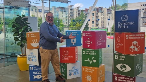 A faculty member posing among boxes decorated with sustainability goals.
