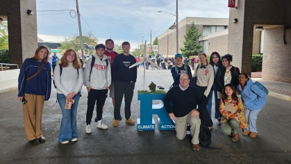 A group of students and a faculty member posing with a 'Climate Action' display.