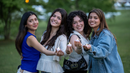 Four people posing together holding one candle each