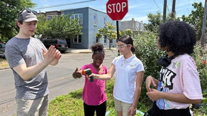 A faculty member talking to 3 kids on a street corner.