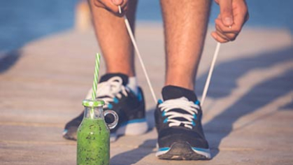 A drink in front of running shoes being tied.