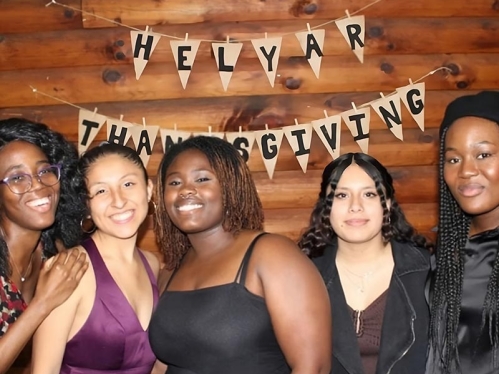 Five students in front of a 'Happy Thanksgiving' sign.